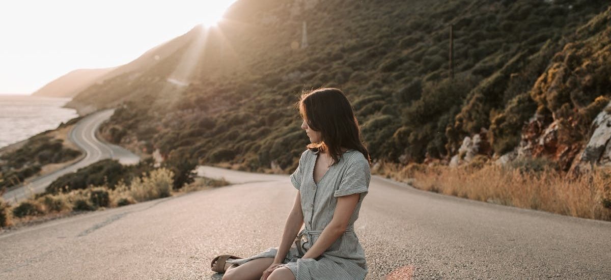 A woman sitting on a coastal road in Antalya during sunset, offering a serene landscape view.