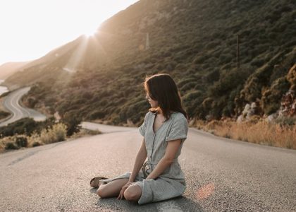 A woman sitting on a coastal road in Antalya during sunset, offering a serene landscape view.